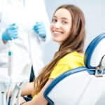 Brunette young woman in a yellow shirt smiles while sitting in a dental chair after soft tissue laser treated her gum disease