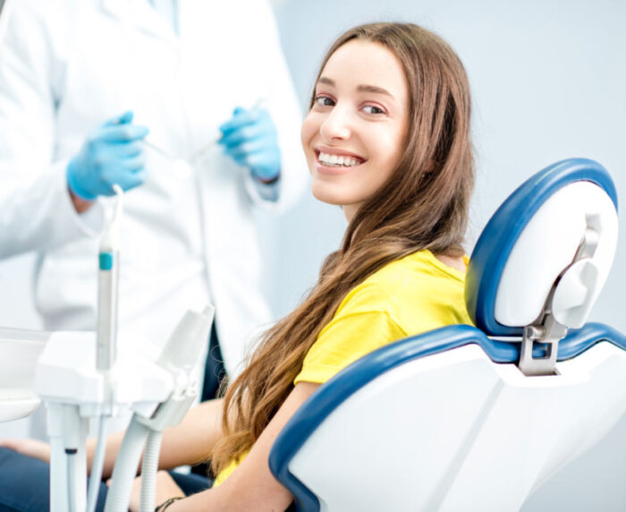 Brunette young woman in a yellow shirt smiles while sitting in a dental chair after soft tissue laser treated her gum disease