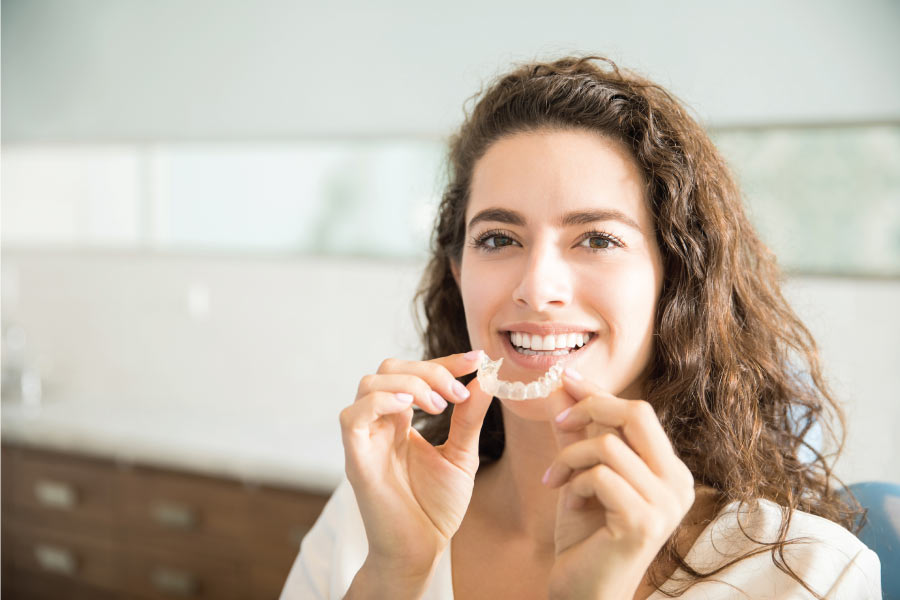 woman smiles while holding her clear aligner with both hands